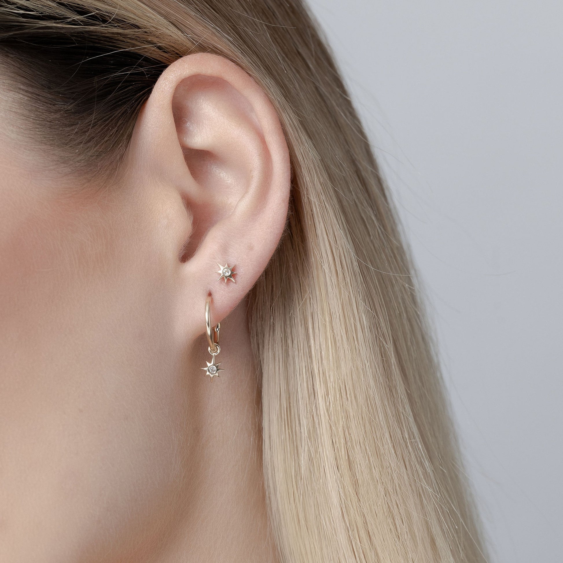 Close-up of a person wearing Silk & Steel gold hoop earrings with star-shaped charms on a neutral background in solid gold.